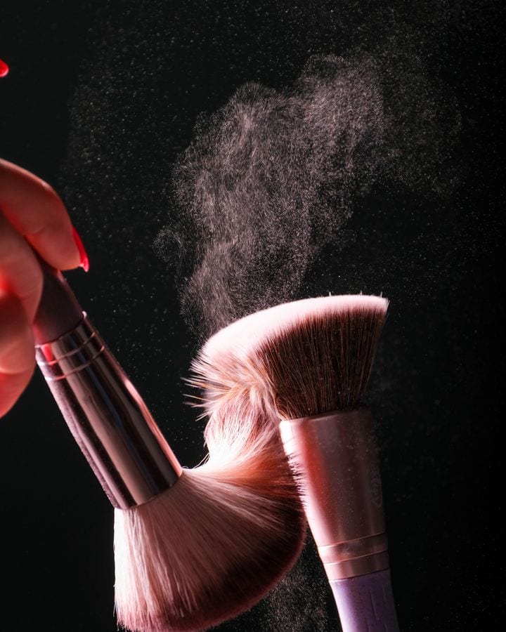 Two brushes tapped together, powder in the air